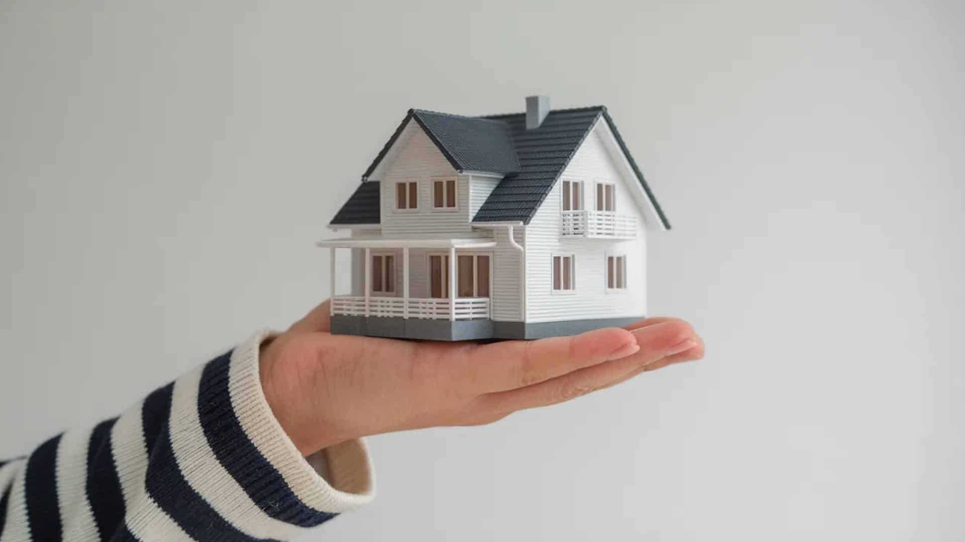 The image shows a hand holding a small model of a house.