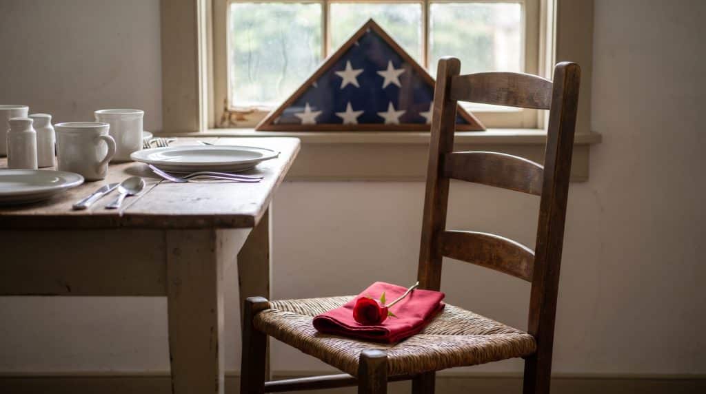An empty chair with a rose and a framed photo honoring a veteran.