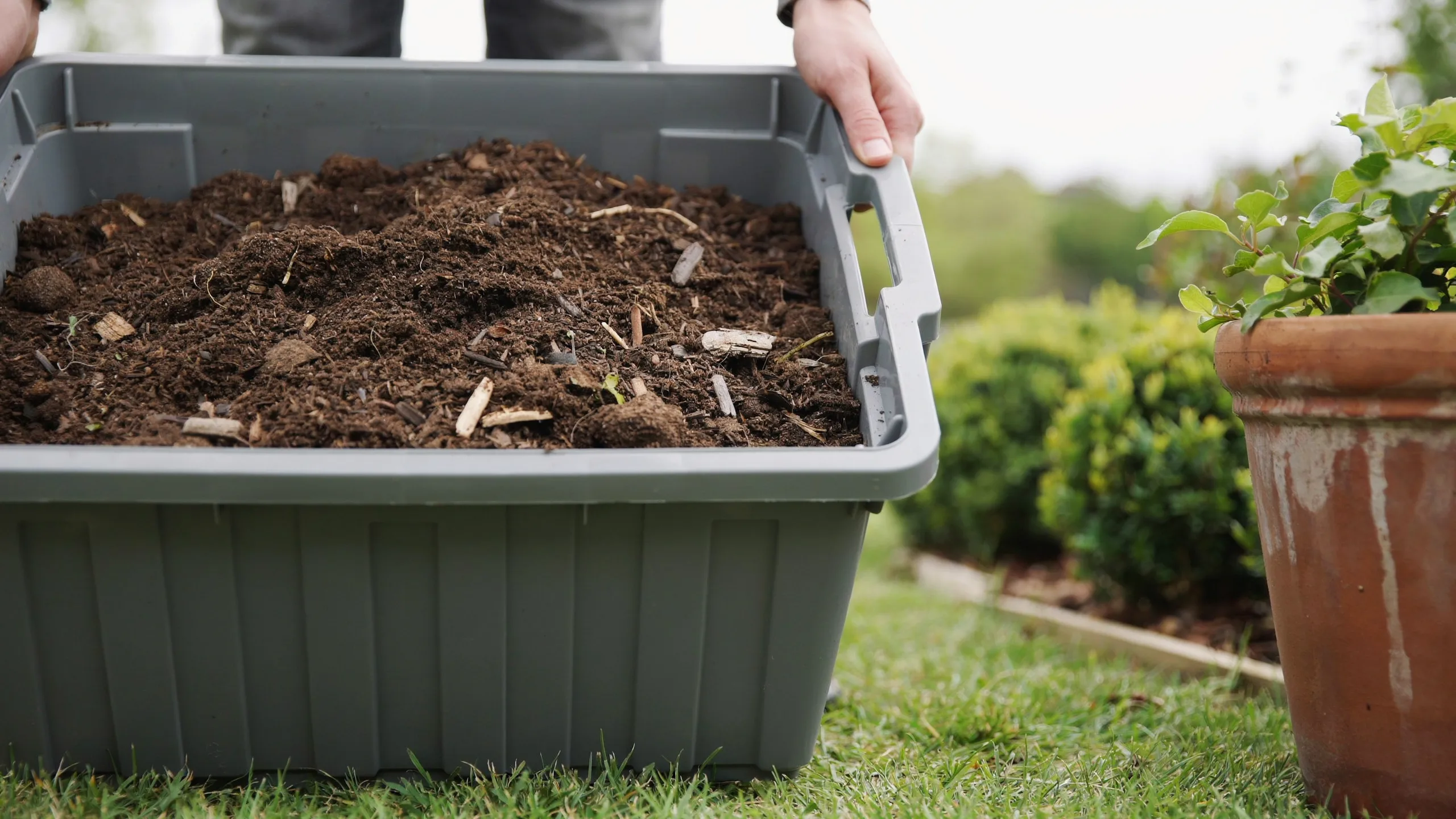 A close-up photograph of a large gray plastic container filled with dark brown compost soil.