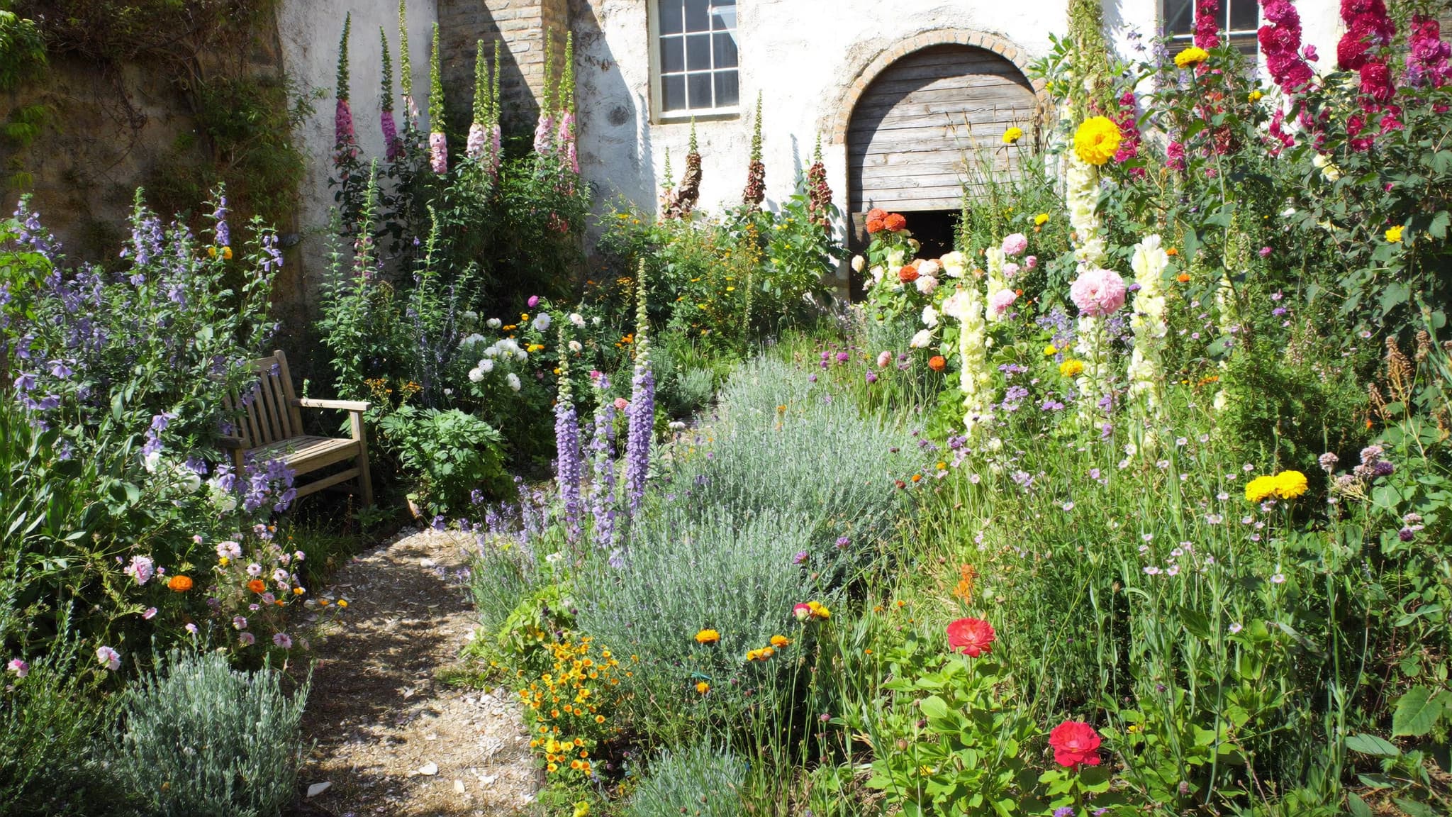 Colorful cottage garden with blooming flowers, lush greenery, and a charming stone pathway.