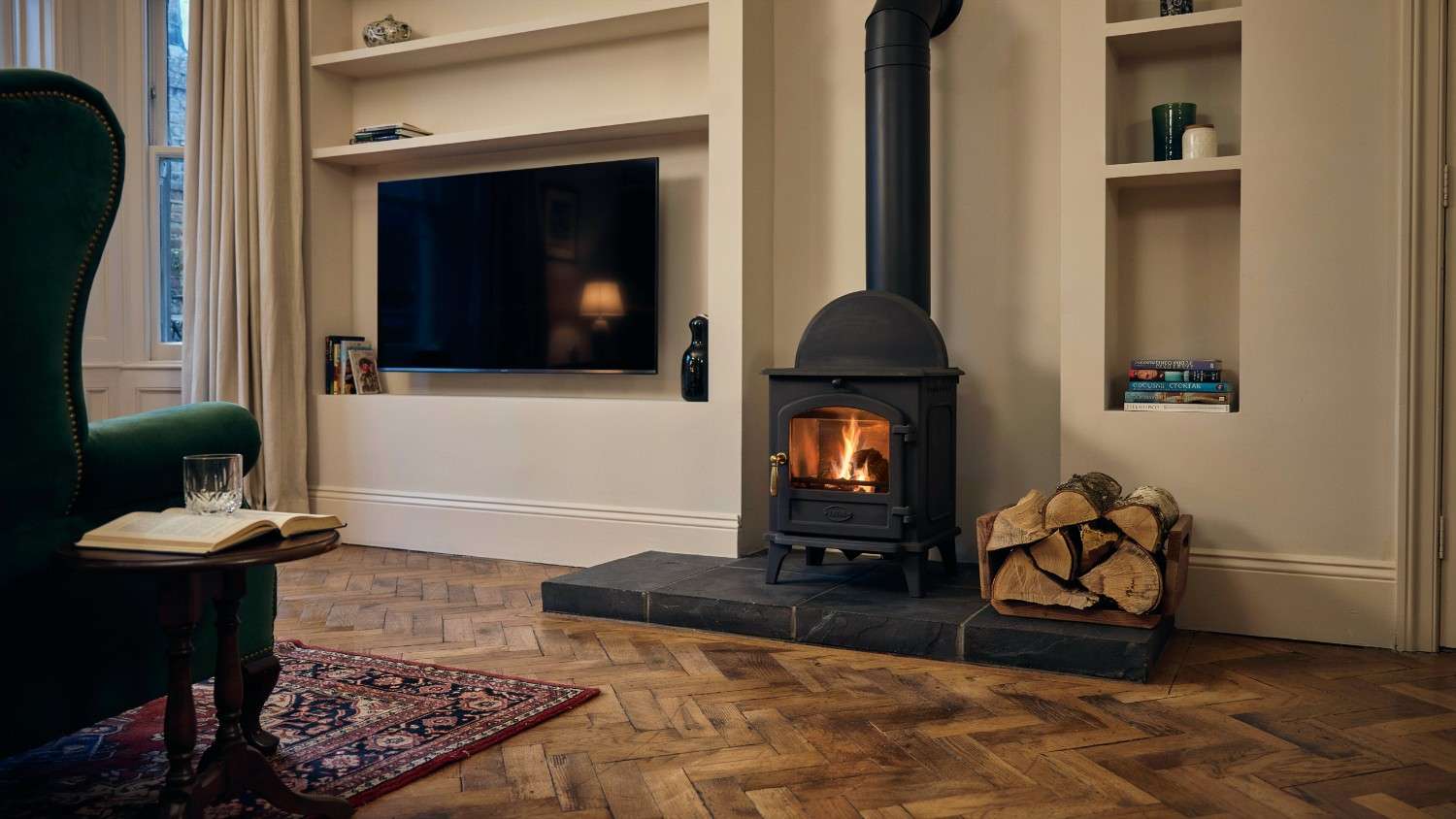 Freestanding cast iron wood burner on a slate hearth with TV mounted on the built-out media wall behind