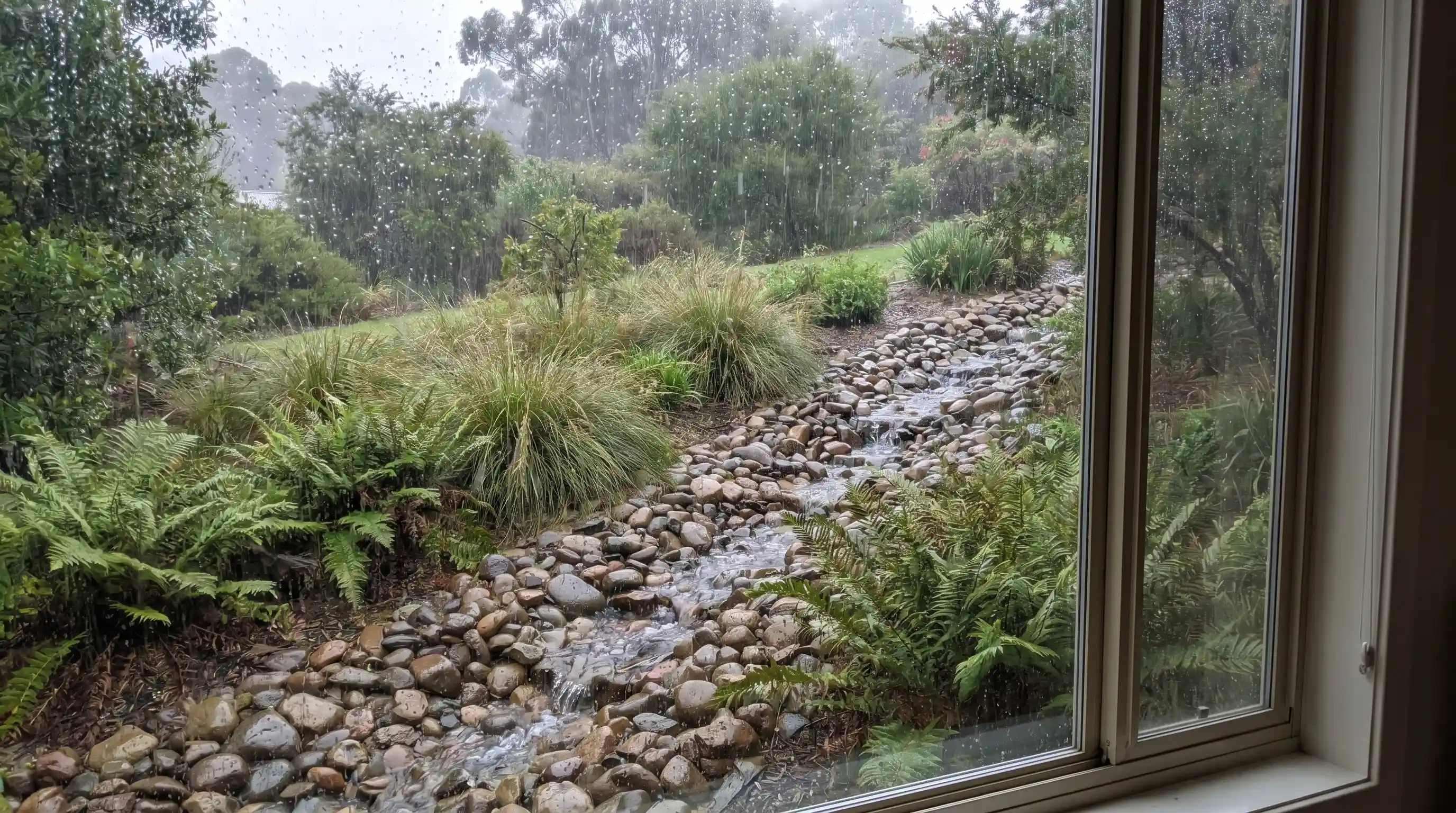 Planted swale directing water flow in a downward sloping garden, bordered by ornamental grasses and shrubs.
