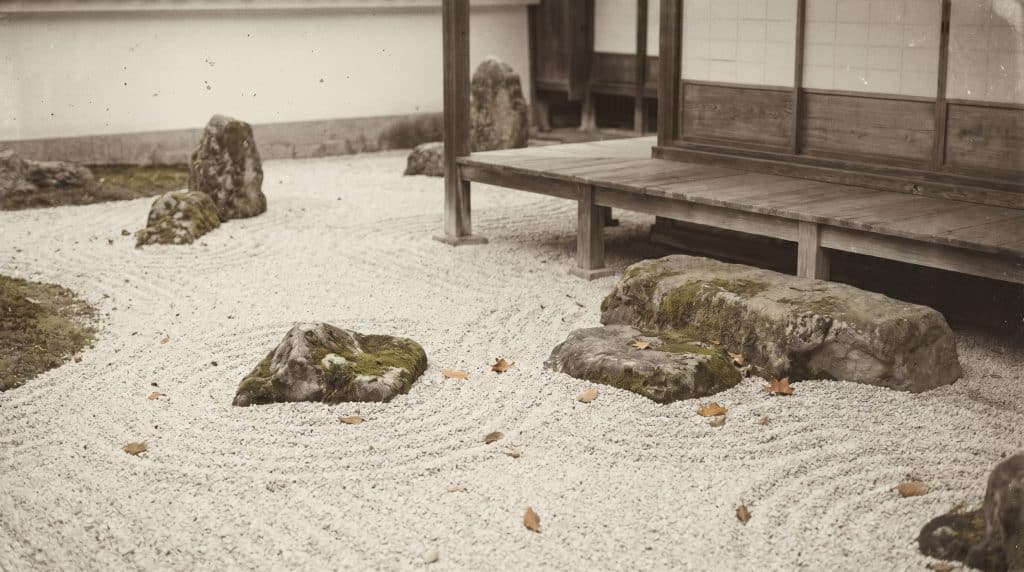 Minimalist Japanese rock garden with scattered stones, raked white gravel, and fallen leaves beside a wooden veranda