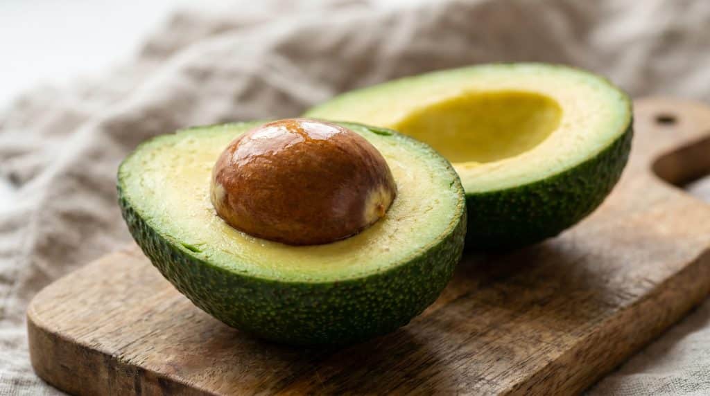 A close-up of an avocado seed inside a halved avocado on a wooden cutting board.