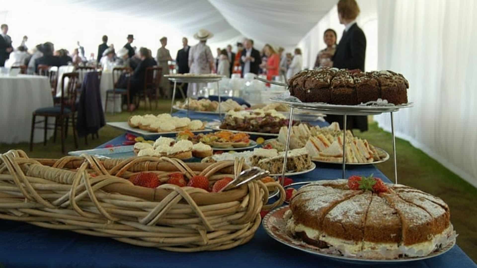 A buffet table inside a marquee featuring wicker baskets of sandwiches and tiered trays of cake.