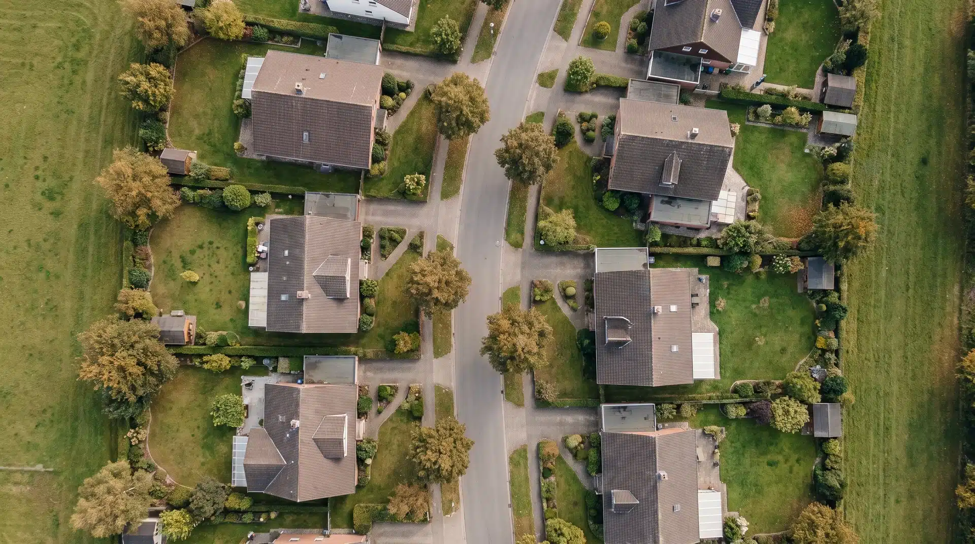 Aerial view of detached houses with open space on all sides on a residential street.