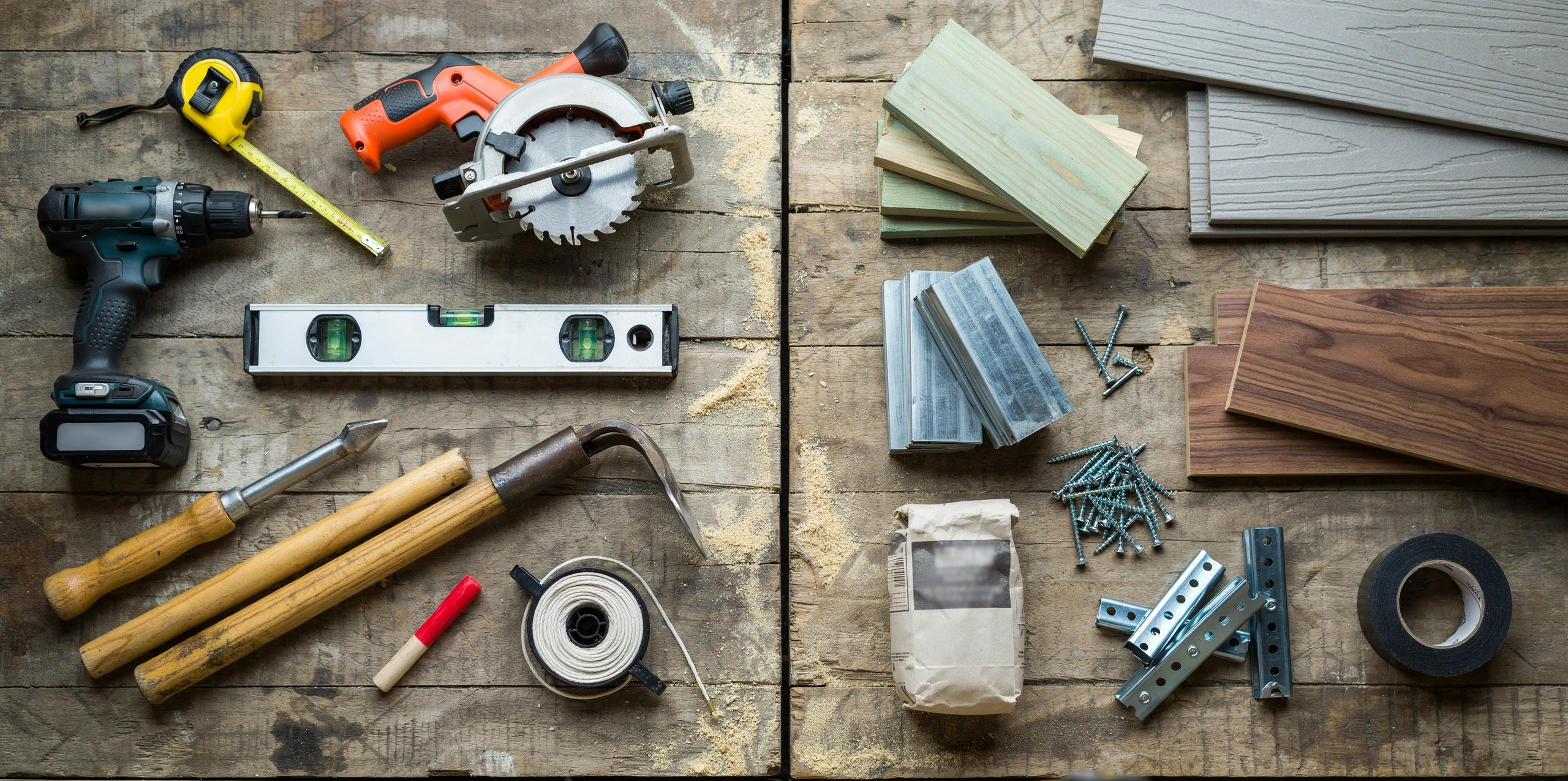 Deck building tools and materials including saw, drill, tape measure, lumber, screws, joists, and concrete footings for construction
