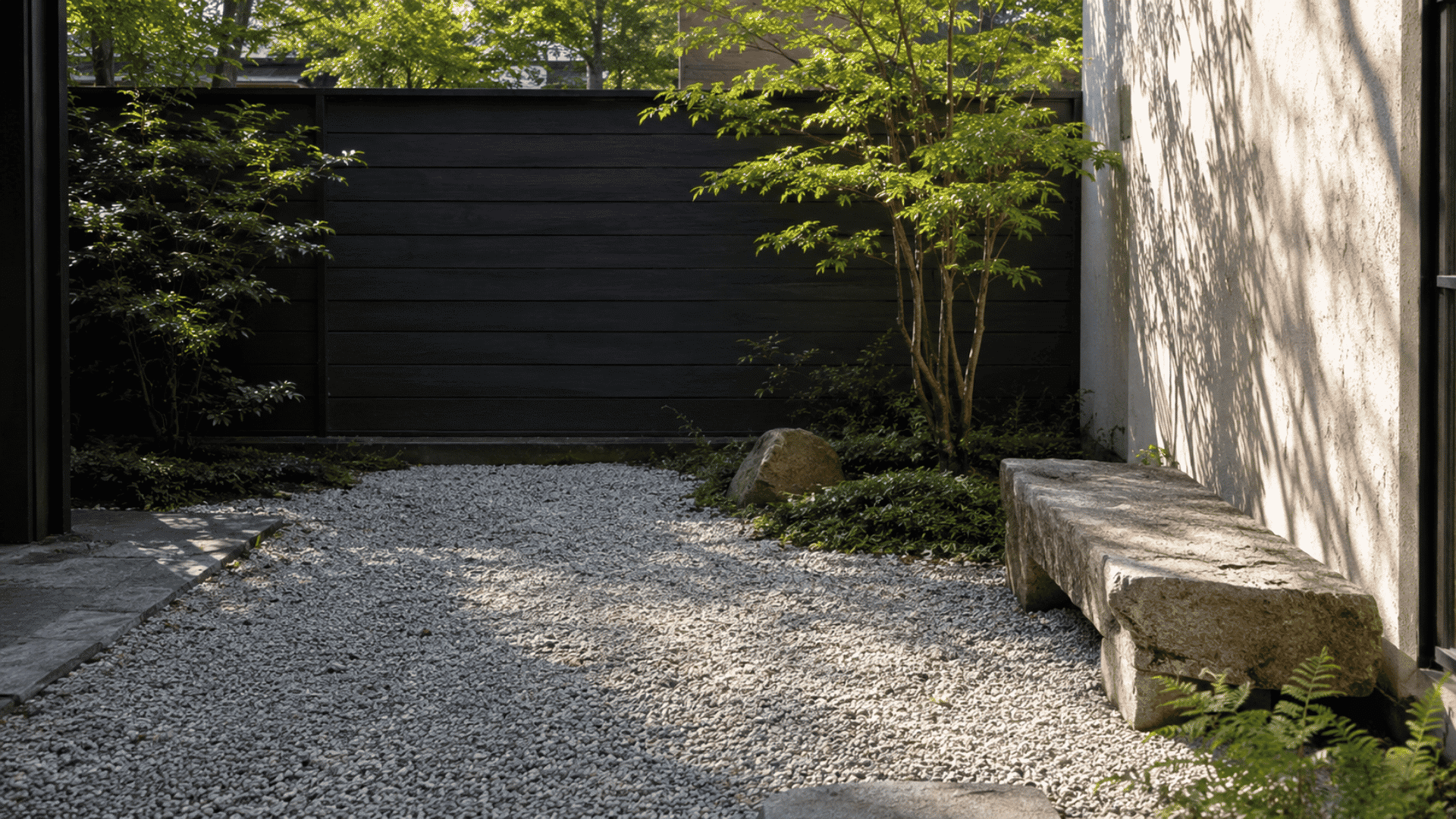 Minimalist pea gravel meditation patio with a stone bench, small maple tree, natural rocks, and soft sunlight.