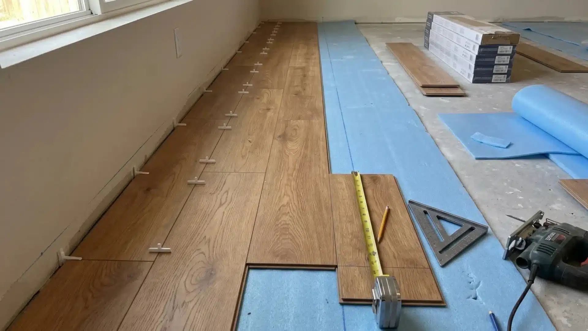 First rows of laminate flooring laid over blue underlay with expansion spacers along the wall.